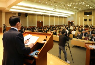 A man at a podium speaking to a room of people there to see the ceremony.
